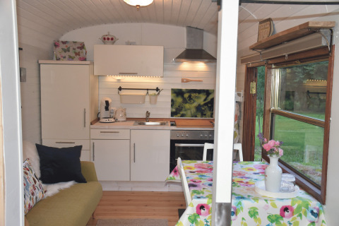 Accogliente interno di una roulotte glamping a Gesundheidshof Denker, con angolo cottura e tavolo vicino alla finestra.