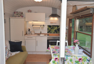 Hyggelig indretning af glamping-vogn på Gesundheidshof Denker, med lille køkken og spisebord ved vindue.