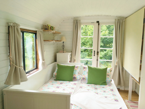 Alojamiento glamping en Zigeunerwagen Jutland, dormitorio luminoso con cama doble y vistas verdes al exterior.