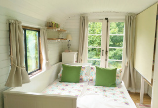 Cozy glamping accommodation in Zigeunerwagen Jutland featuring a bright bedroom, double bed and leafy views outside.