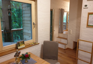 Interieur van glampingverblijf 'Boomhut - Mainbaumhaus' met hout, groot raam en zicht op het groen.