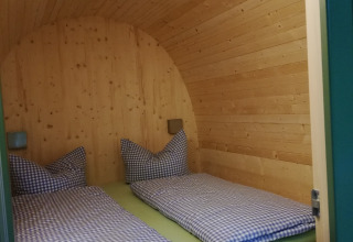 Alojamiento glamping Boomhut - Mainbaumhaus con techo de madera curvo y dos camas individuales con ropa a cuadros.