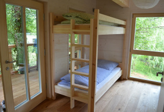 Binnenaanzicht van Boomhut - Mainbaumhaus met stapelbedden, houten vloer en grote ramen richting bos.