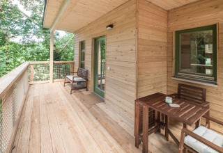 Wooden terrace with chairs and table at glamping accommodation 'Boomhut - Mainbaumhaus' in a lush forest setting.