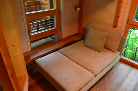 Interno di un alloggio glamping in casa sull'albero con poltrona comoda e grandi finestre sulla natura.