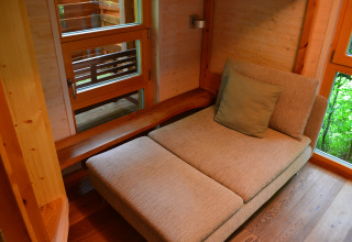 Interieur van een luxe boomhut glamping accommodatie met comfortabele stoel en ramen met bosuitzicht.