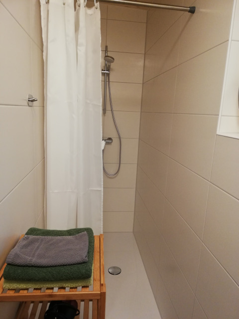 Modern shower area in Boomhut glamping accommodation with white curtain, tiled walls, and green towels.