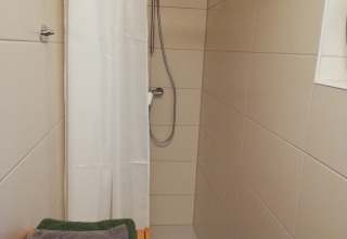 Douche moderne dans un hébergement glamping Boomhut avec rideau blanc et serviettes vertes pliées.