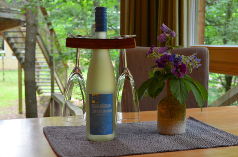 Bouteille de vin, deux verres et vase de fleurs sur une table dans un hébergement glamping dans un arbre.