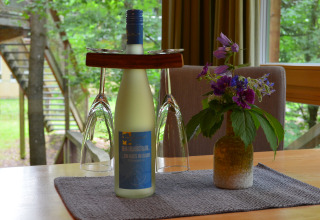 Weiße Weinflasche mit zwei Gläsern und Blumenstrauß auf Tisch in Glamping-Unterkunft im Baumhaus.