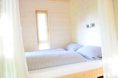 Lichte, knusse slaapkamer met tweepersoonsbed en geruit beddengoed in Boomhut - Mainbaumhaus glamping.