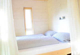Lichte, knusse slaapkamer met tweepersoonsbed en geruit beddengoed in Boomhut - Mainbaumhaus glamping.