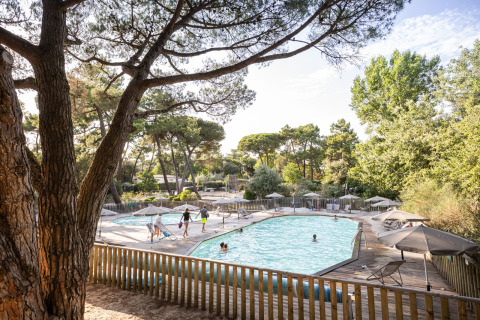 Piscina rodeada de árboles y sombrillas en Huttopia Chardons Bleus – Ile de Ré Glamping en Nouvelle-Aquitaine.