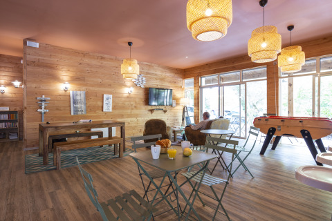 Espace commun chaleureux à Huttopia Chardons Bleus – Ile de Ré avec murs en bois, canapés et baby-foot.