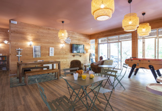 Espace commun chaleureux à Huttopia Chardons Bleus – Ile de Ré avec murs en bois, canapés et baby-foot.