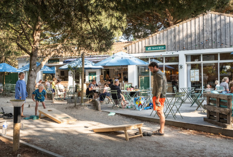 Udendørs caféområde ved Huttopia Chardons Bleus – Ile de Ré glampingplads med familier der spiller spil.