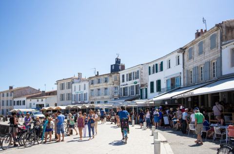 Belebte Straße bei Huttopia Chardons Bleus – Ile de Ré mit Menschen, Fahrrädern und Cafés unter Sonne.