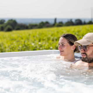 Twee personen ontspannen in een bubbelbad met uitzicht op wijngaarden bij Camping La Grappe Fleurie - Glamping Beaujolais.