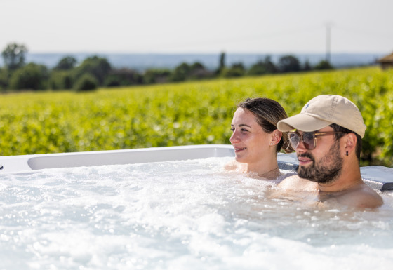 Due persone si rilassano in una vasca idromassaggio con vista sui vigneti al Camping La Grappe Fleurie - Glamping Beaujolais.