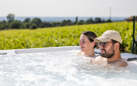 Twee personen ontspannen in een bubbelbad met uitzicht op wijngaarden bij Camping La Grappe Fleurie - Glamping Beaujolais.