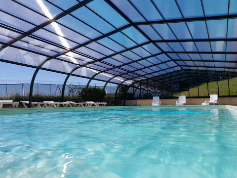 Camping La Grappe Fleurie - Glamping Beaujolais, piscina cubierta con tumbonas y agua azul reluciente.