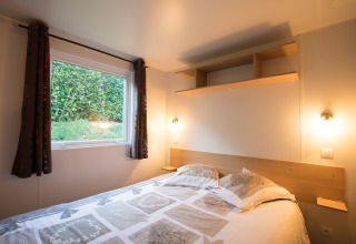 Gemütliches Schlafzimmer im Glamping-Zelt von Camping La Grappe Fleurie - Glamping Beaujolais mit Doppelbett und Ausblick ins Grüne.