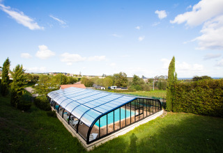 Überdachtes Schwimmbecken bei Camping La Grappe Fleurie - Glamping Beaujolais, eingebettet in grüne Landschaft.