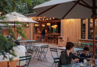 Zona de comedor exterior con mesas verdes en Camping Huttopia De Veluwe, luces cálidas al atardecer.