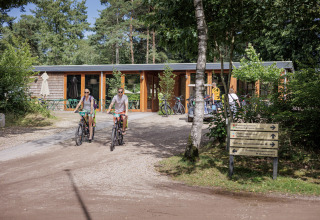 Two people ride bicycles at Camping Huttopia De Veluwe, a glamping site in Gelderland surrounded by trees.