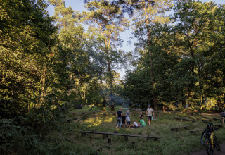 Familie rond kampvuur in het bos bij Camping Huttopia De Veluwe – Glamping tenten in Gelderland.