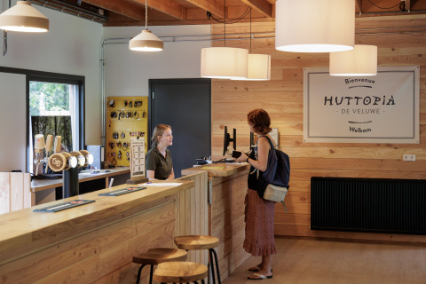 Reception desk at Camping Huttopia De Veluwe, with two people, wood decor, and a welcoming environment.