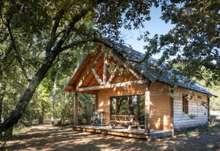 Gemütliche Holzhütte im Grünen bei Village Huttopia Sud Ardèche – Glamping Ardèche, umgeben von Bäumen.