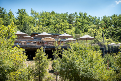 Buitenterras met parasols tussen groen bij Village Huttopia Sud Ardèche – Glamping Ardèche.