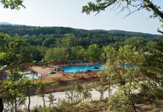 Vue sur la piscine parmi les arbres et collines au Village Huttopia Sud Ardèche – Glamping Ardèche, France.