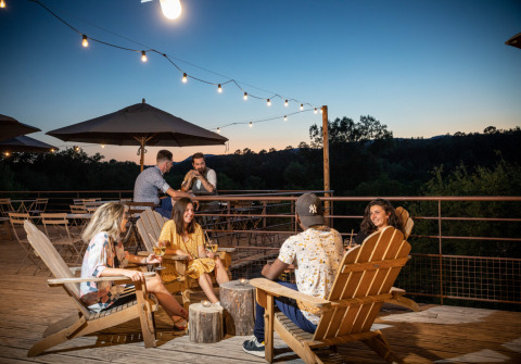 Gruppe venner nyder aftenen udendørs med drinks på Village Huttopia Sud Ardèche – Glamping Ardèche.