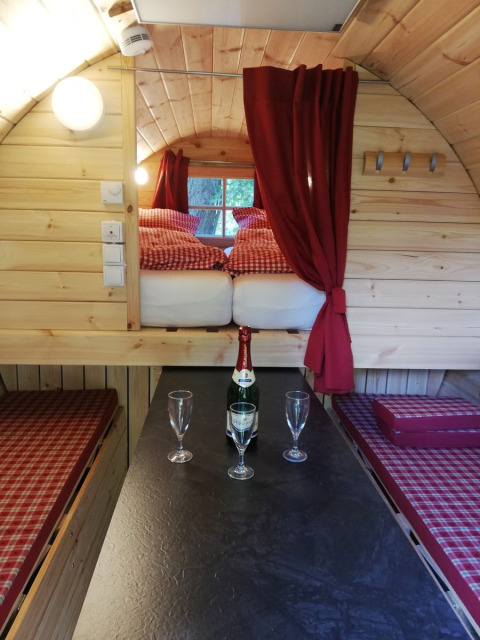 Vista interna di una botte glamping al Camping Hetzingen con letto, tavolo, champagne e calici.