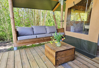 Udendørs sofa og bord med blomster på træterrasse ved safaritelte på Minicamping Sint Jan i Zeeland.
