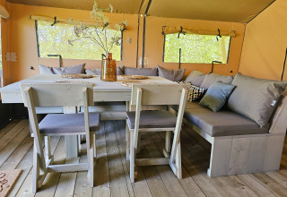 Interno di una tenda safari di lusso al Minicamping Sint Jan con zona pranzo accogliente e ampie finestre.
