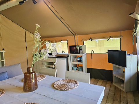 Vista interna di una tenda safari a Minicamping Sint Jan, Zelanda, con tavolo da pranzo, angolo cottura e TV.