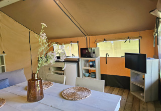Innenansicht eines Safarizelts auf Minicamping Sint Jan in Zeeland mit Esstisch, Küche und Fernseher.