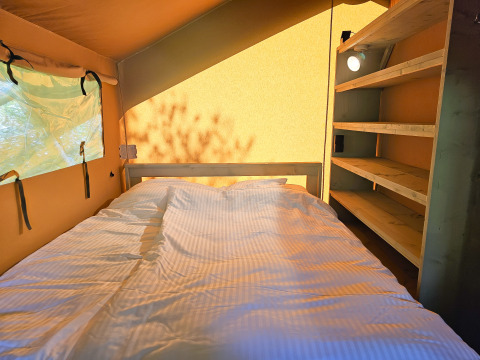 Vista interna di una tenda safari con letto e scaffali presso Minicamping Sint Jan - Safaritenten Zeeland.