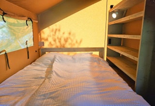 Binnenkant van een safaritent met bed en planken bij Minicamping Sint Jan - Safaritenten Zeeland.