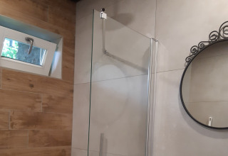 Douche de salle de bain moderne, porte en verre, miroir rond et petite fenêtre au Minicamping Sint Jan, Zeeland.