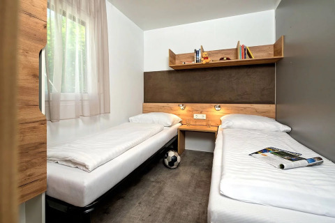 Moderne Glamping-Unterkunft mit zwei Einzelbetten, Regal, natürlichem Licht und minimalistischem Design.