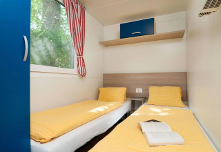 Moderne glampingaccommodatie met twee eenpersoonsbedden, geel beddengoed en raam bij Wellnesscamping & Landhuis Parth - Stacaravans Oostenrijk.