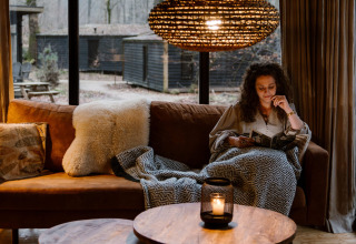 Vrouw leest op een gezellige bank in een Buitenplaats Beekhuizen boshut op de Veluwe, Nederland.