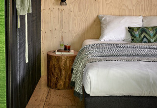 Sistemazione glamping accogliente con pareti in legno, letto e comodino a tronco a Buitenplaats Beekhuizen, Veluwe.