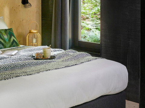 Forest cabin glamping at Buitenplaats Beekhuizen Veluwe, featuring a cozy bed and forest views out the window.
