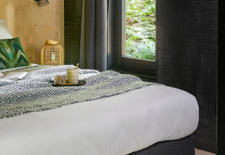 Glamping forest cabin bij Buitenplaats Beekhuizen in Veluwe, met gezellig bed en uitzicht op het groene bos.