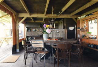 Vue intérieure d’un hébergement de glamping rustique avec table en bois, chaises et cuisine ouverte à Woodlodges Noord-Holland.